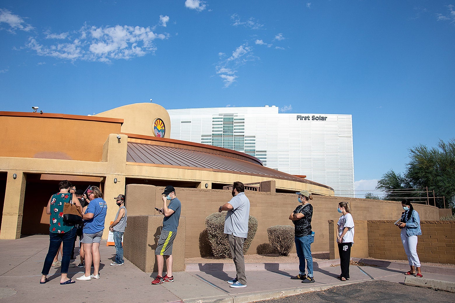 Voters wait in a spaced-out line outside a theater on a sunny day.