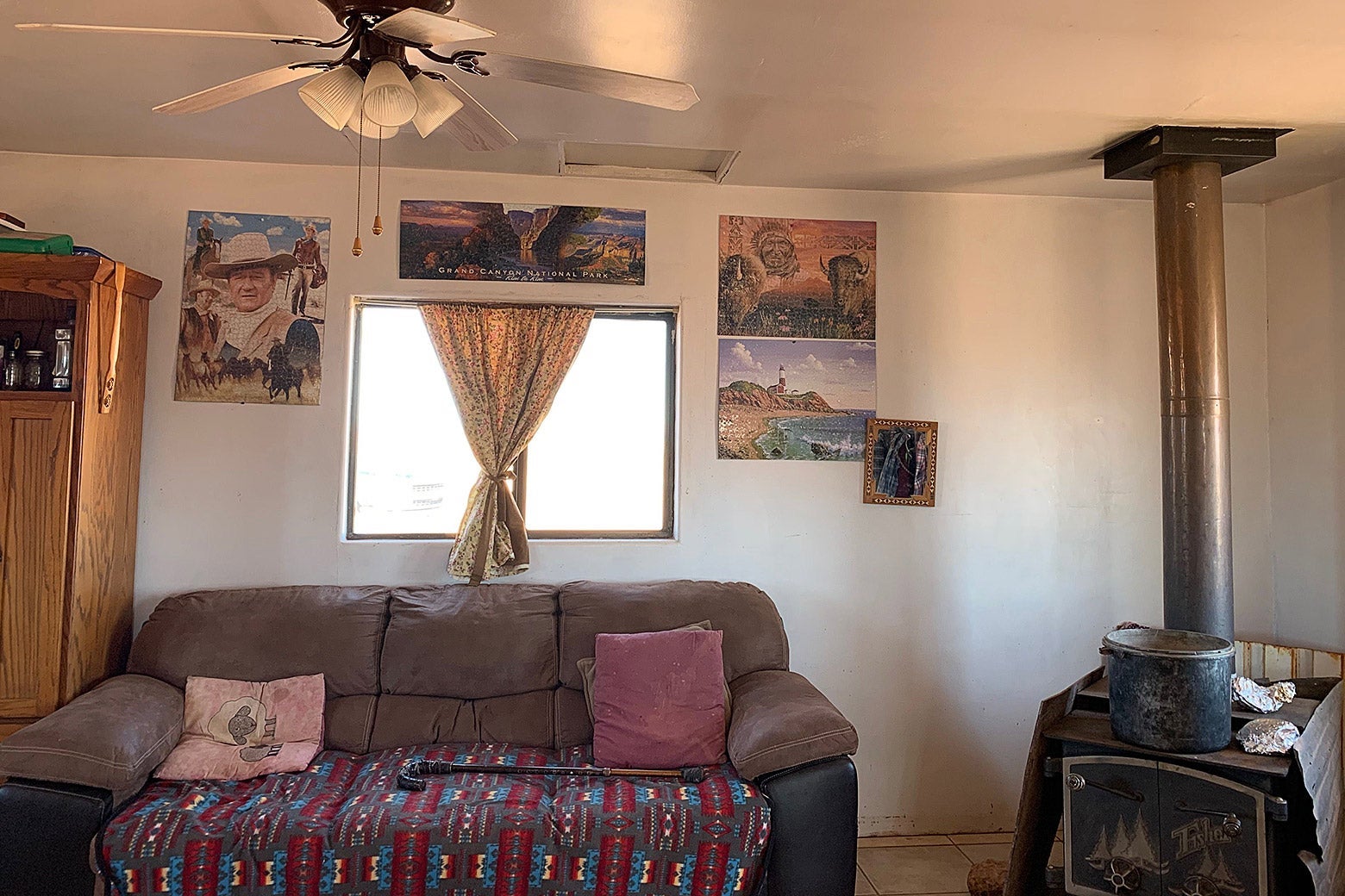 A couch sits under a window, next to a wood-burning stove. Puzzles depicting Western scenes are attached to the wall surrounding the window.