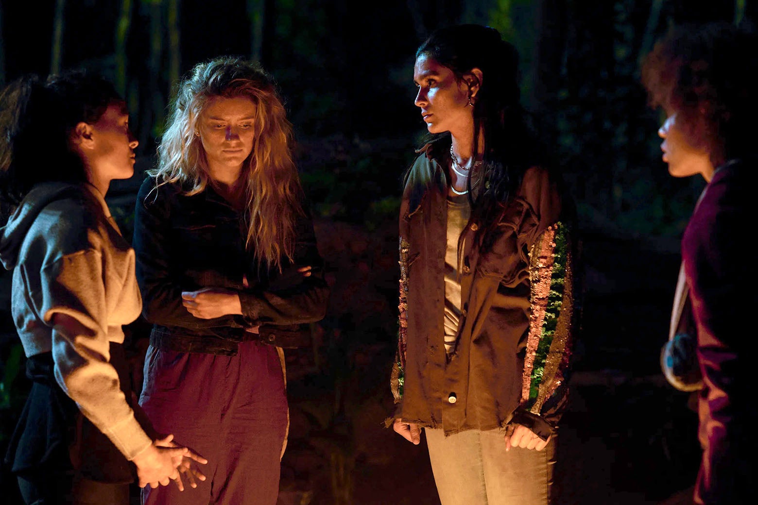 Four young women stand in the glow of a campfire at night.