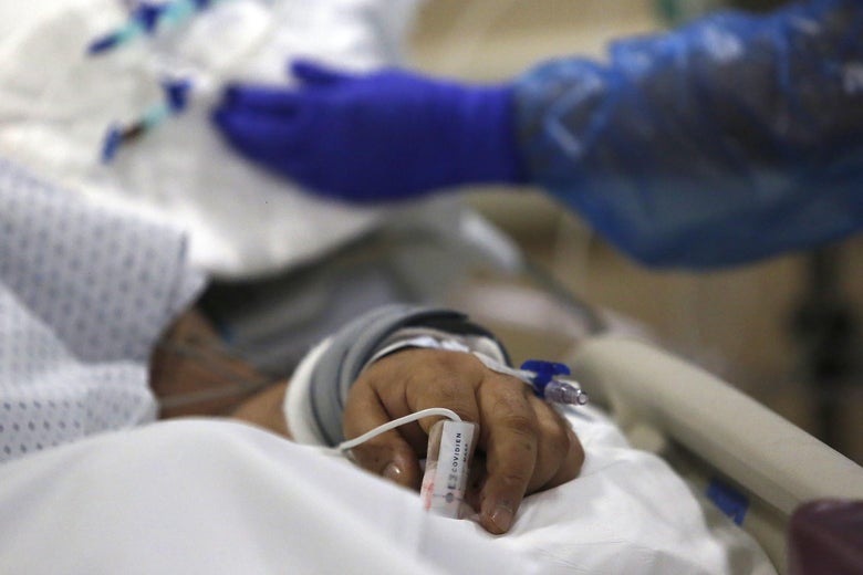 A close-up of a patient's hand on a hospital bed as gloved hands work nearby.