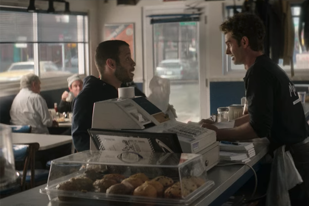 Robin de Jesus and Andrew Garfield face each other across a diner counter in the foreground while James C. Nicola and Roger Bart dine at a table in the background. 