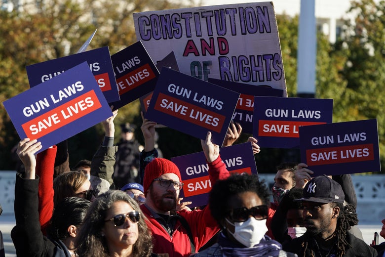 A crowd of protesters carrying signs reading "Gun laws save lives"