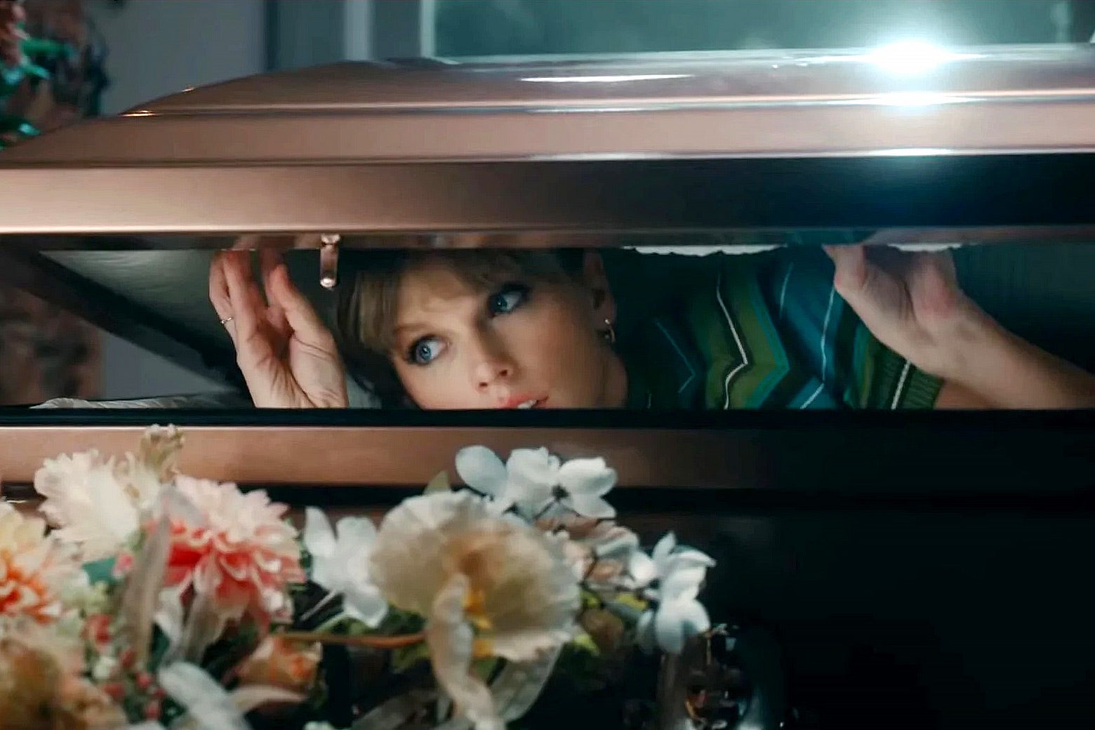 Taylor Swift peaks out of a shiny casket.
