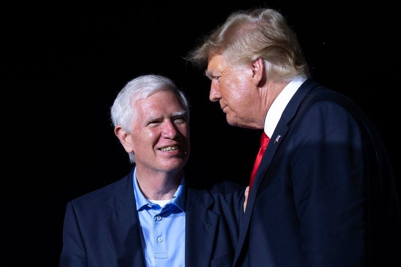 The white-haired Brooks, wearing a blue blazer over a polo shirt, stands next to Trump against a black background.