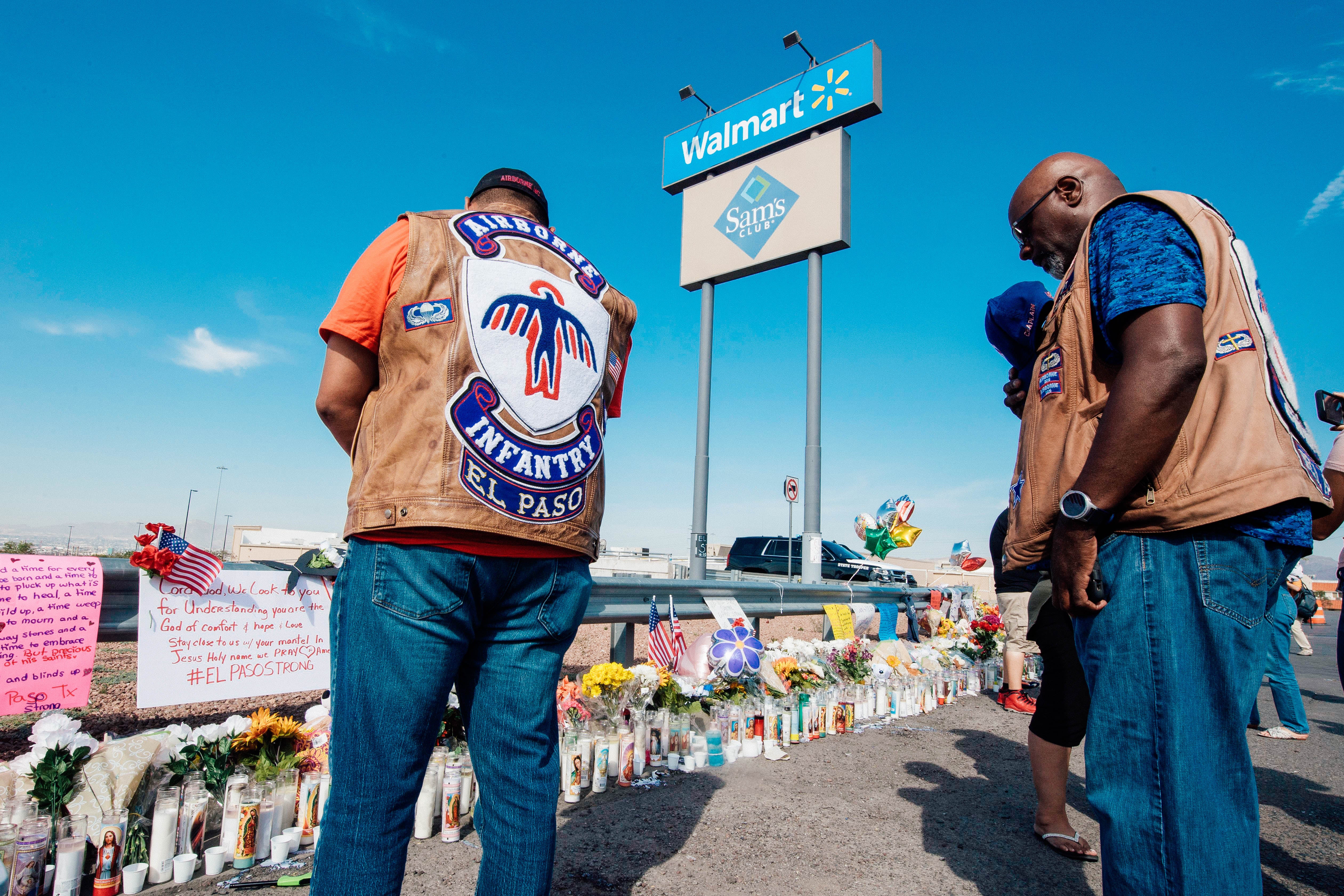 People in motorcycle gear bow their heads in prayer before a memorial of flowers and signs of support for the shooting victims.