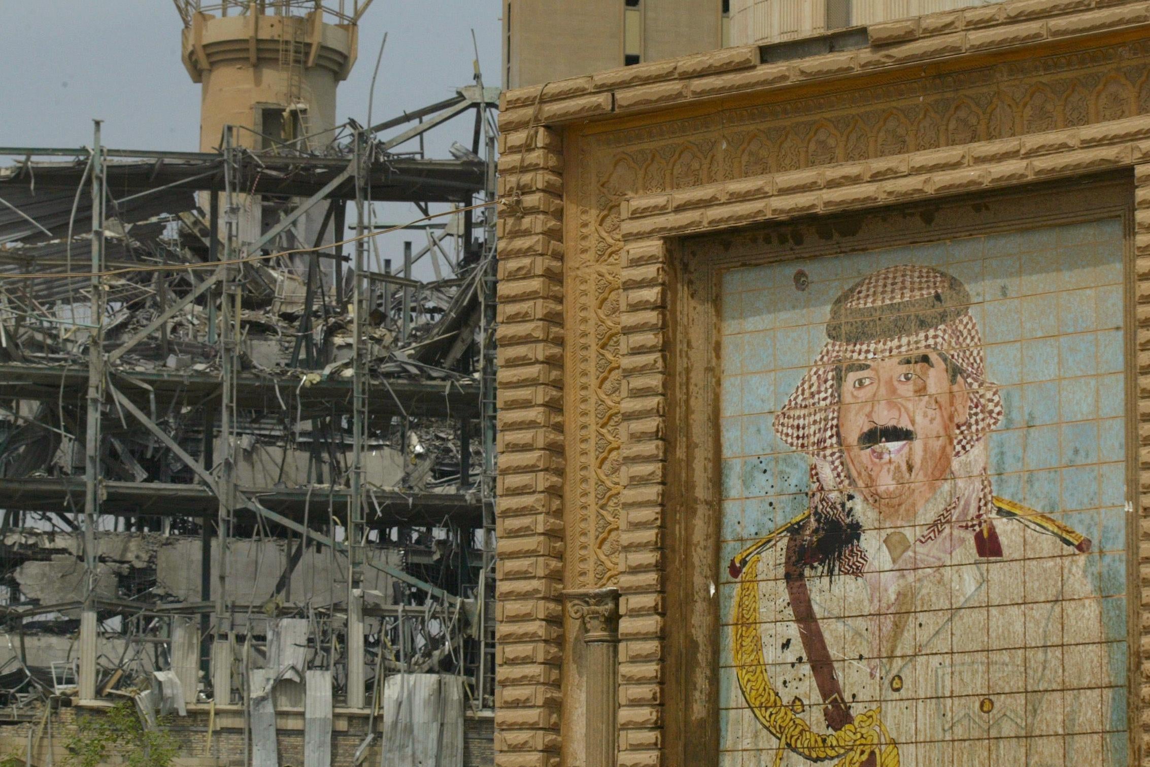A damaged mural of Iraq’s ousted leader Saddam Hussein in a military outfit, next to a destroyed building in Baghdad 