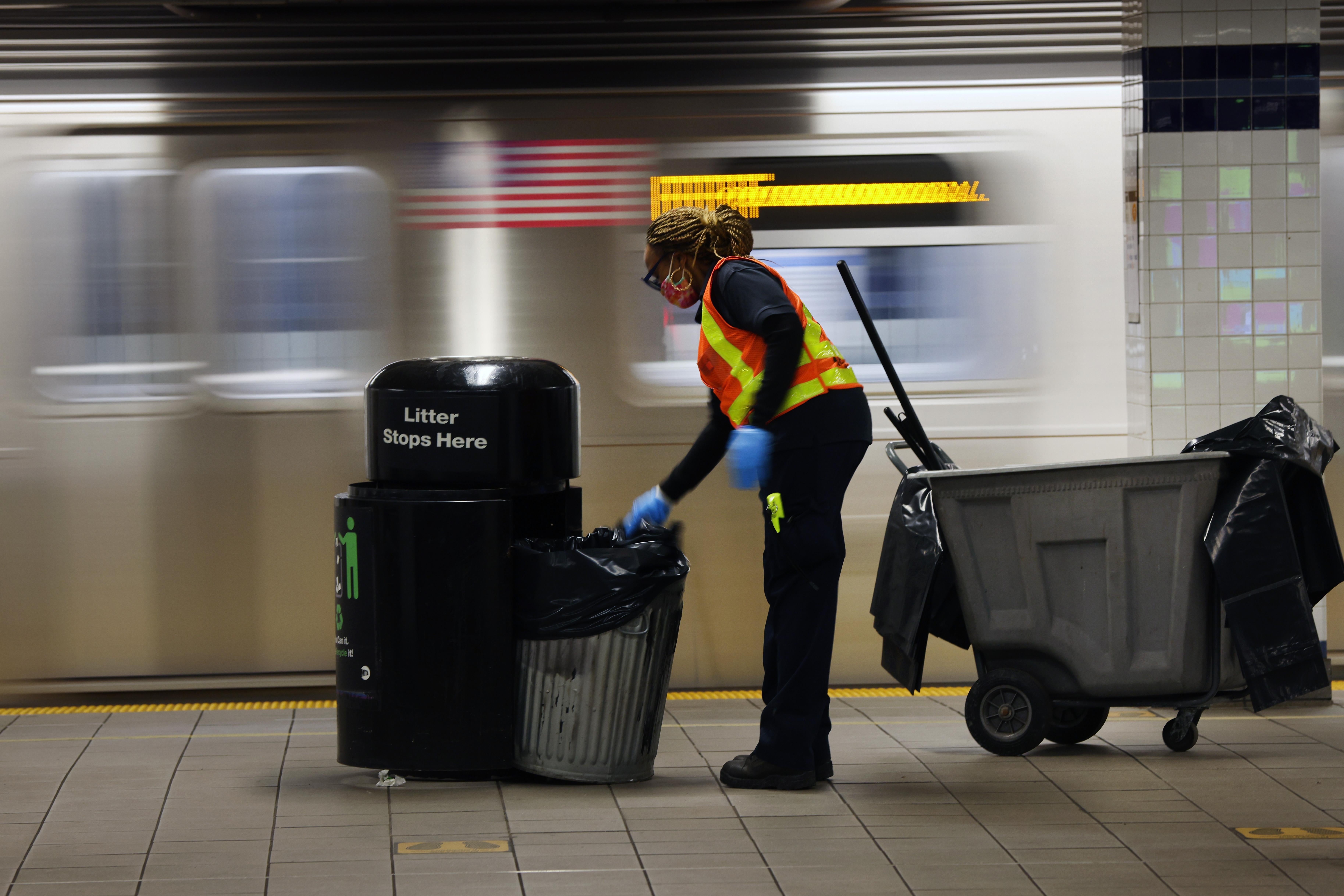 A woman empties trash on a subway platform.