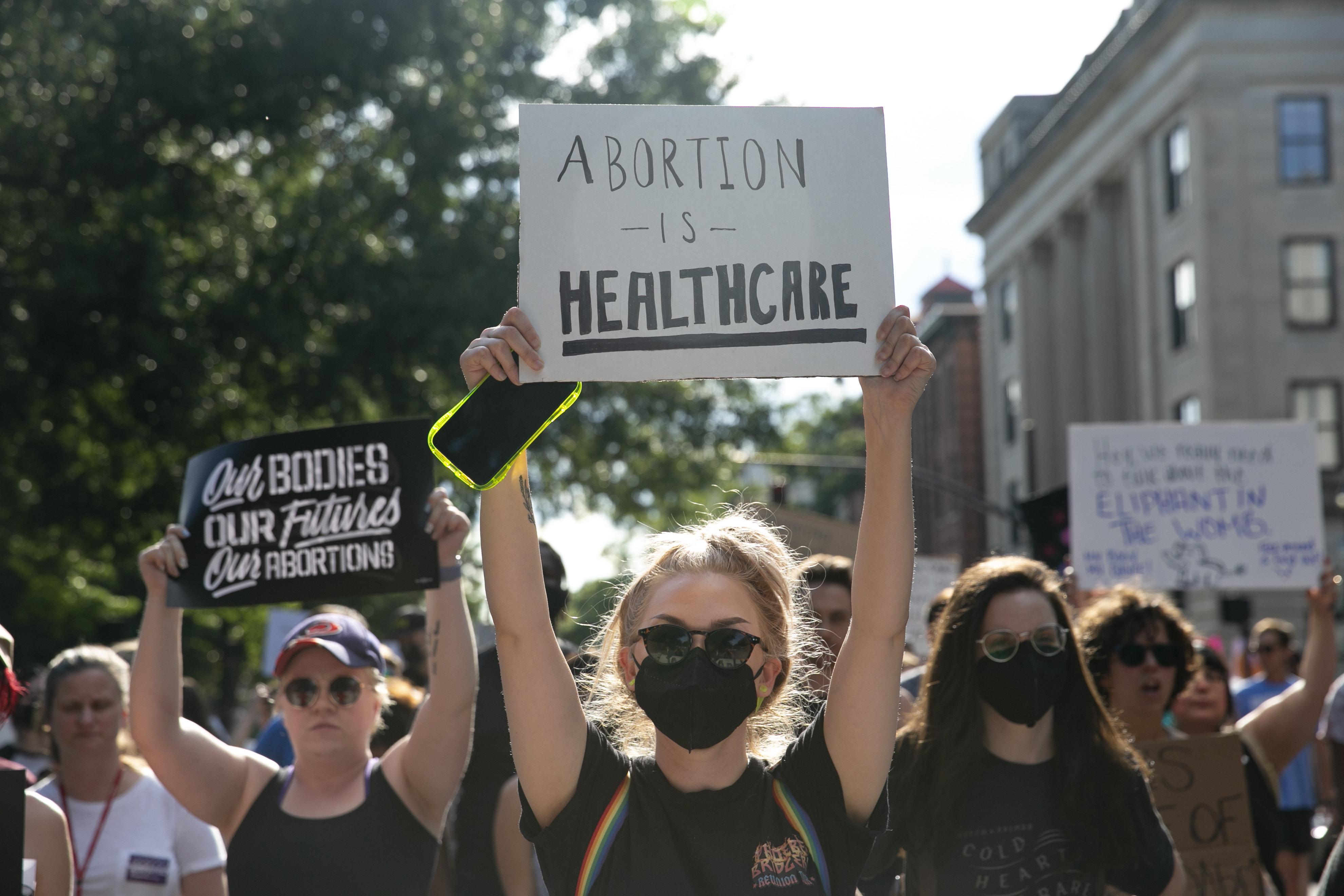Protesters holding up signs saying "Abortion is Healthcare" and "Our Bodies, Our Futures, Our Abortions."
