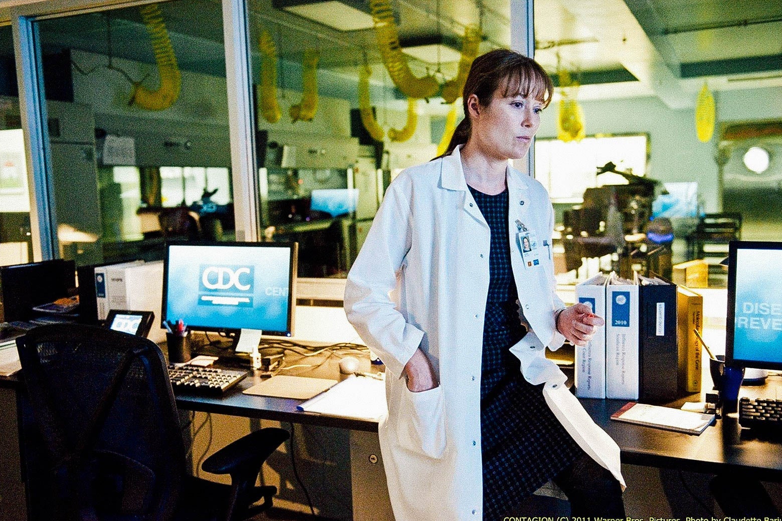 A white-coated female scientist is seen a laboratory. A computer behind her reads "CDC."
