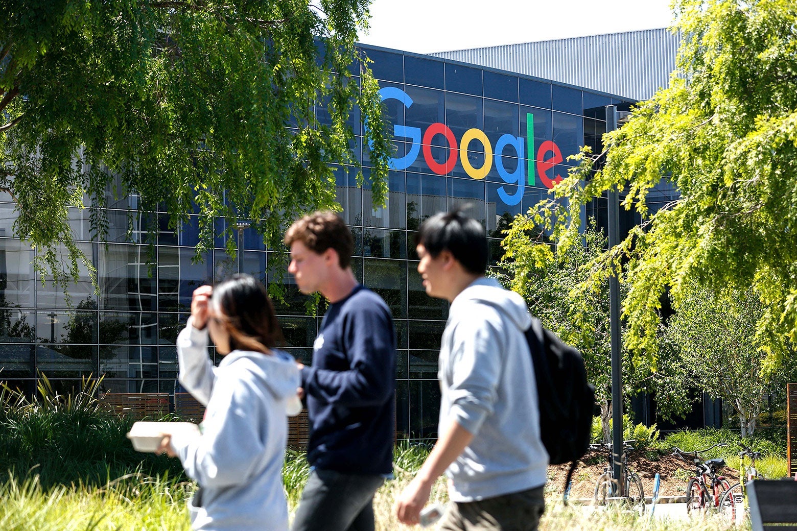 Three workers wearing sweatshirts converse and walk outside Google headquarters.