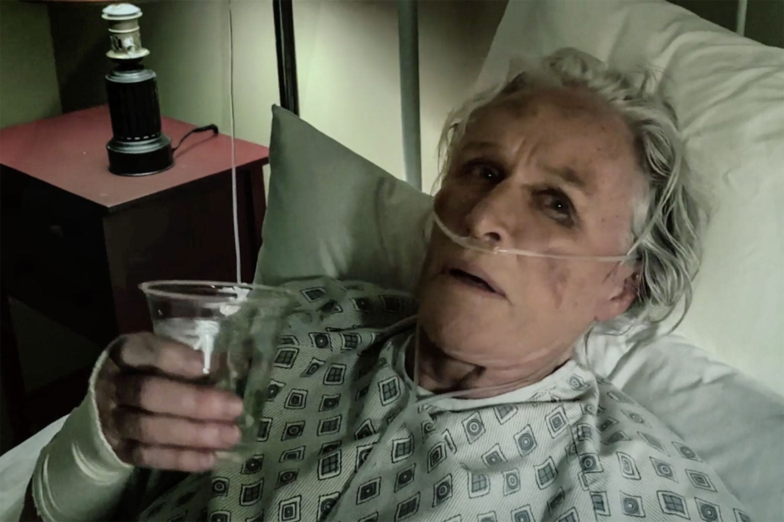 Glenn Close in a hospital bed wearing a hospital gown.