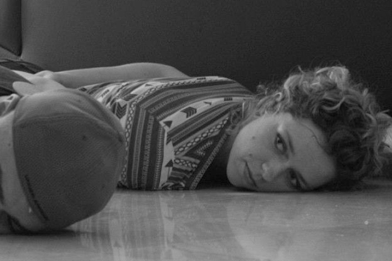 A black-and-white photo of a woman lying on the ground with her face to a tile floor.
