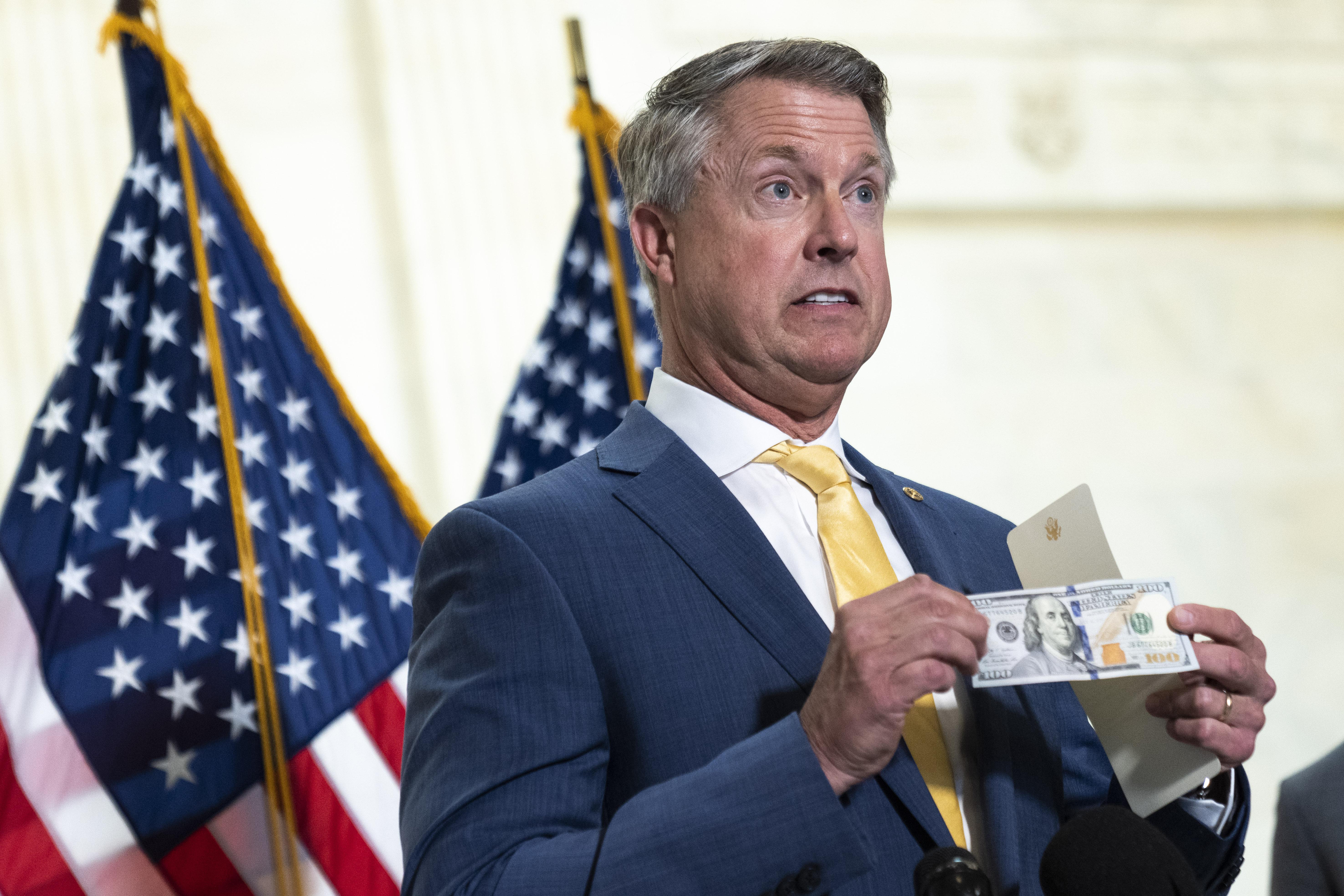 Roger Marshall holds up a $100 bill while standing in front of two U.S. flags.