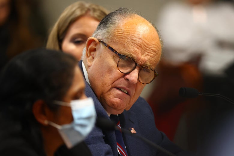 Rudy Giuliani, not wearing a mask, looks beside him at a woman in a surgical mask.