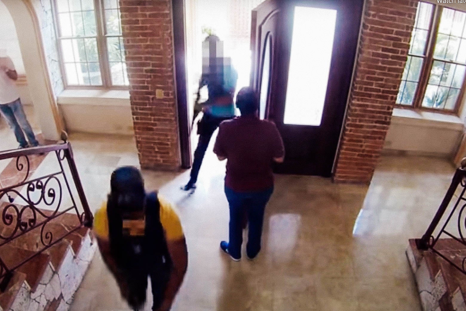 A housekeeper opens the door to a house as local authorities enter with guns and bulletproof vests.