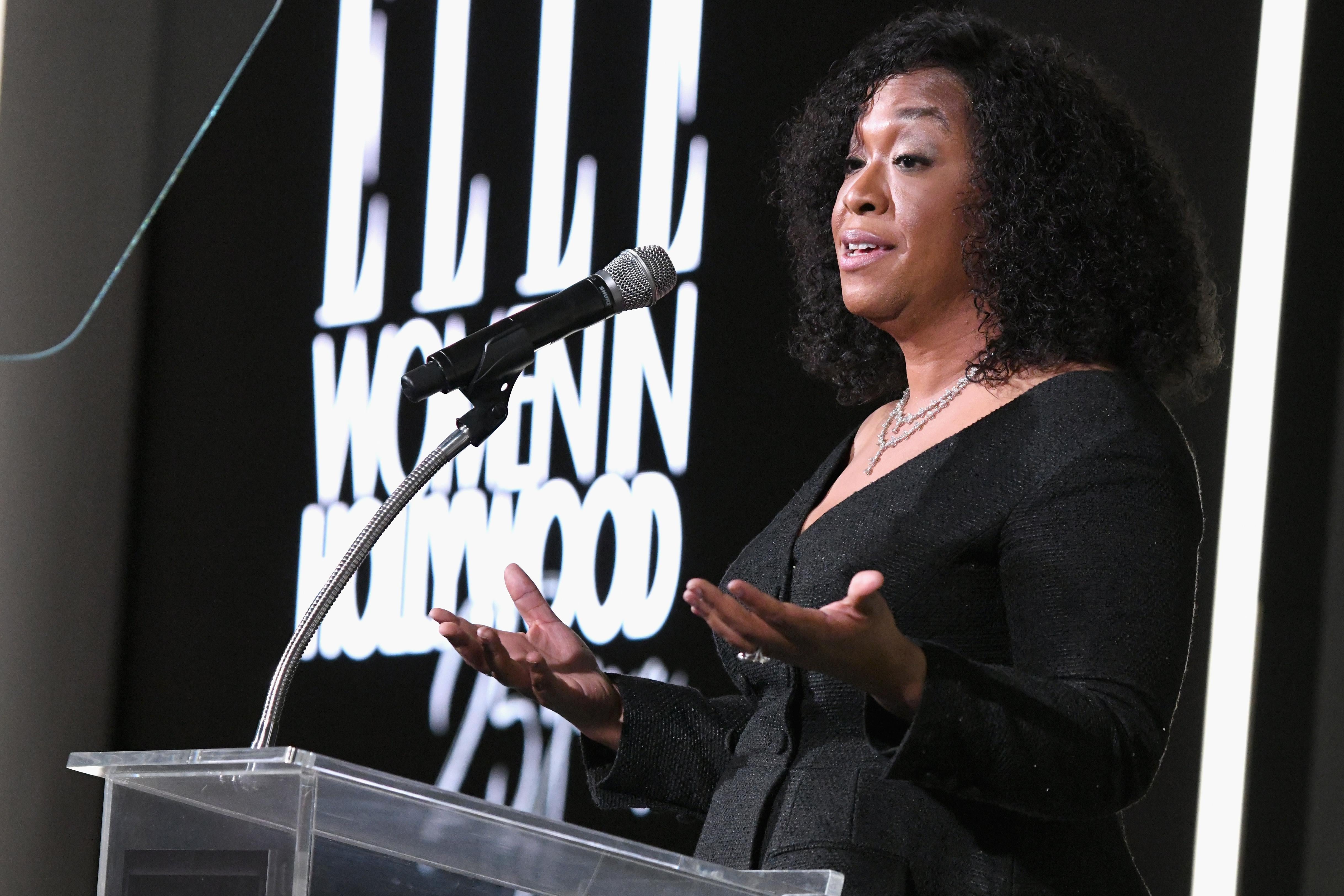 Shonda Rhimes stands at a glass podium, arms outstretched.