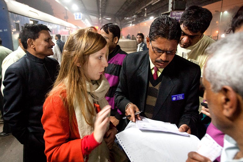 Kim Wall, within a crowd, is seen talking to a man holding and looking down at some papers.