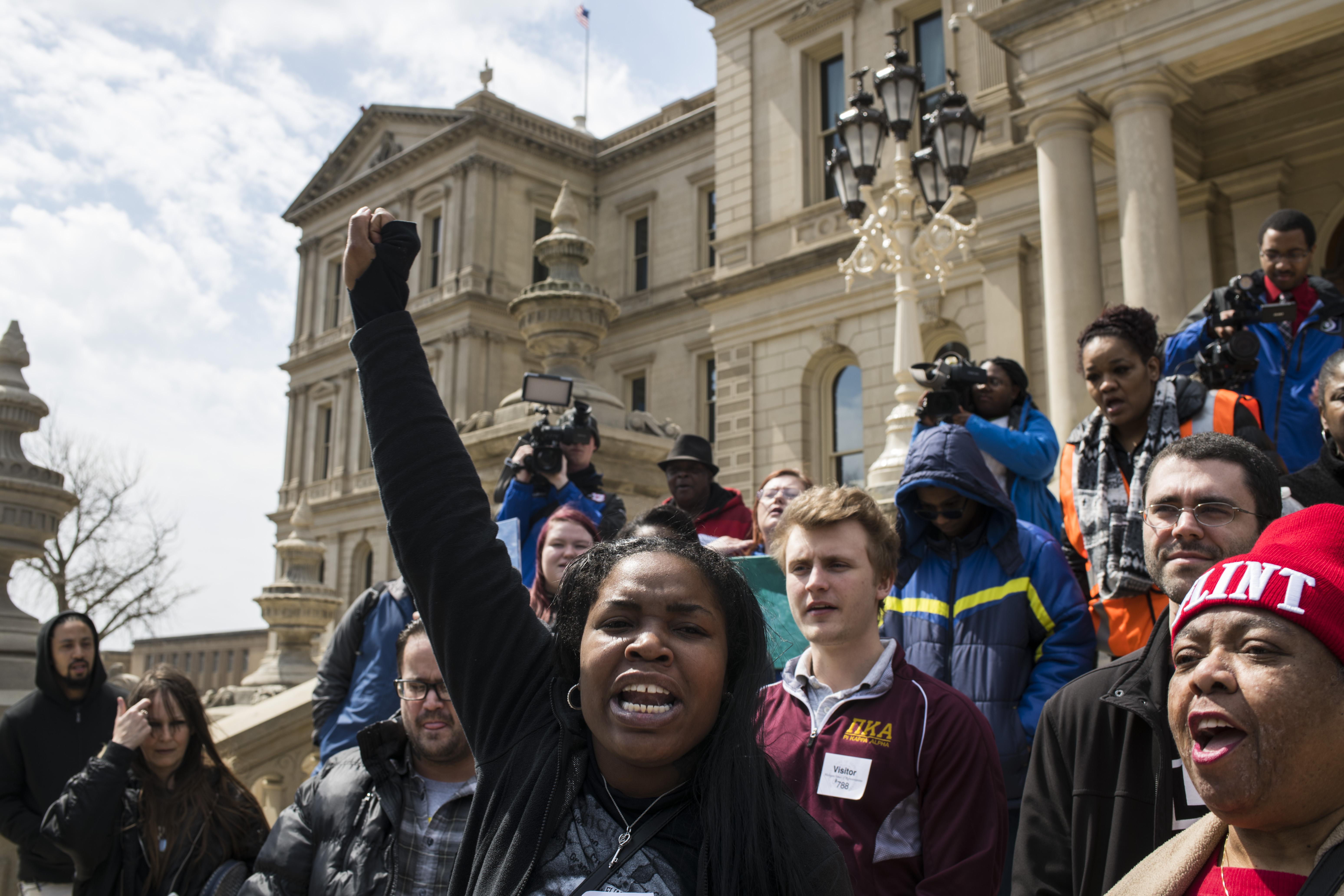 Protesters hold up their fists and chant on the steps of the Michigan state Capitol.