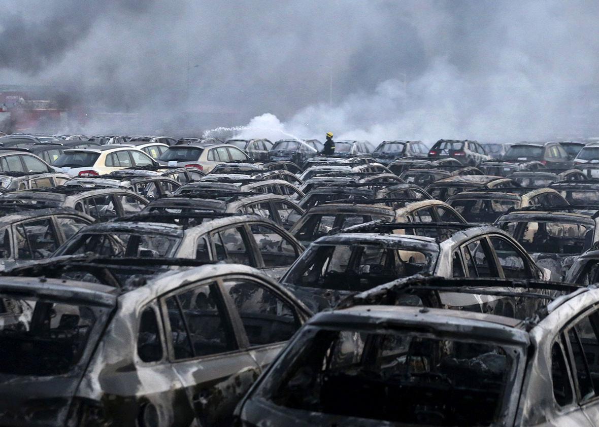 A firefighter works at the site near damaged vehicles as smoke rises from the debris after the explosions at the Binhai new district in Tianjin, China.