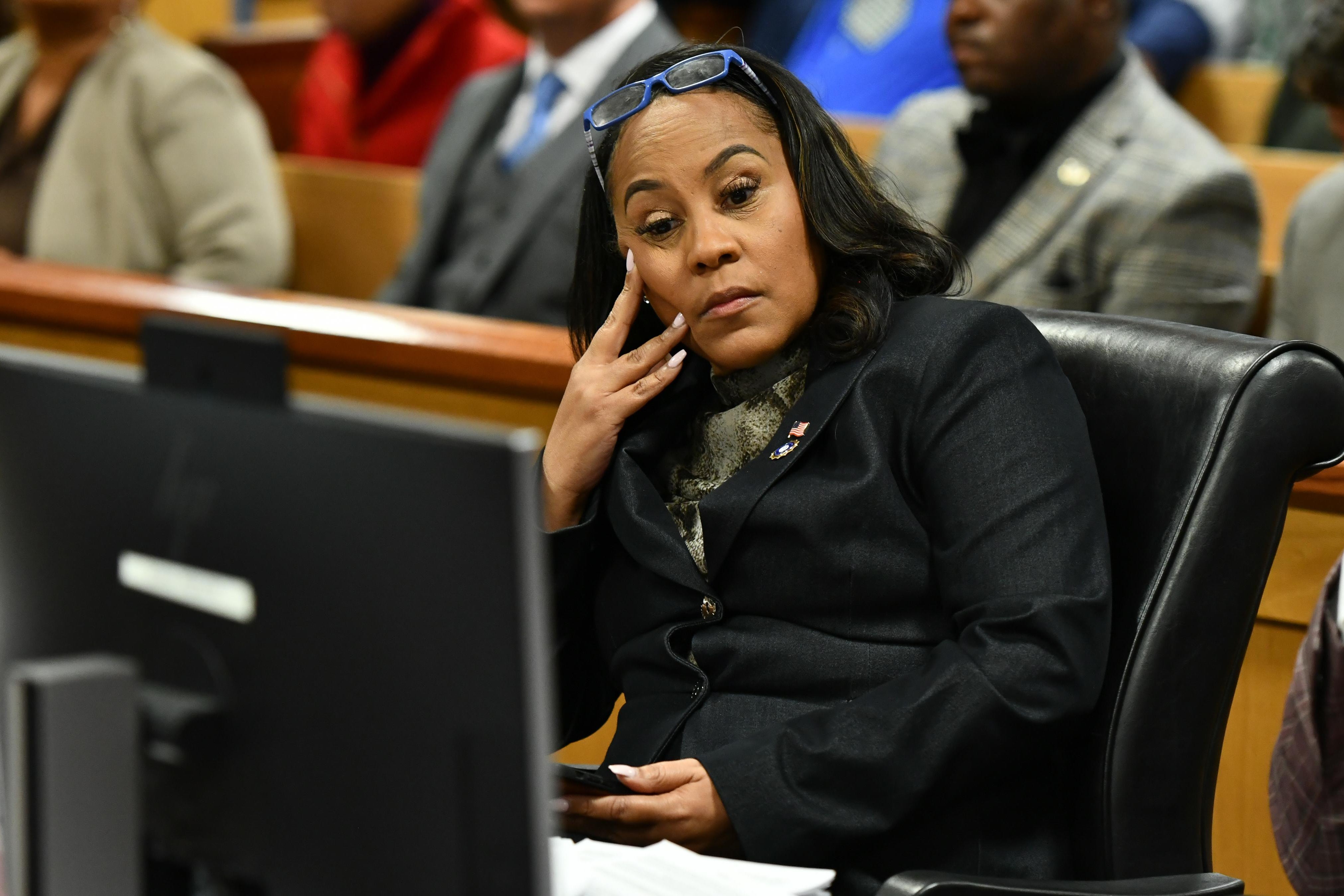 Fulton County District Attorney Fani Willis rests her face against her hand as she sits in court during a hearing in the 2020 election interference case.