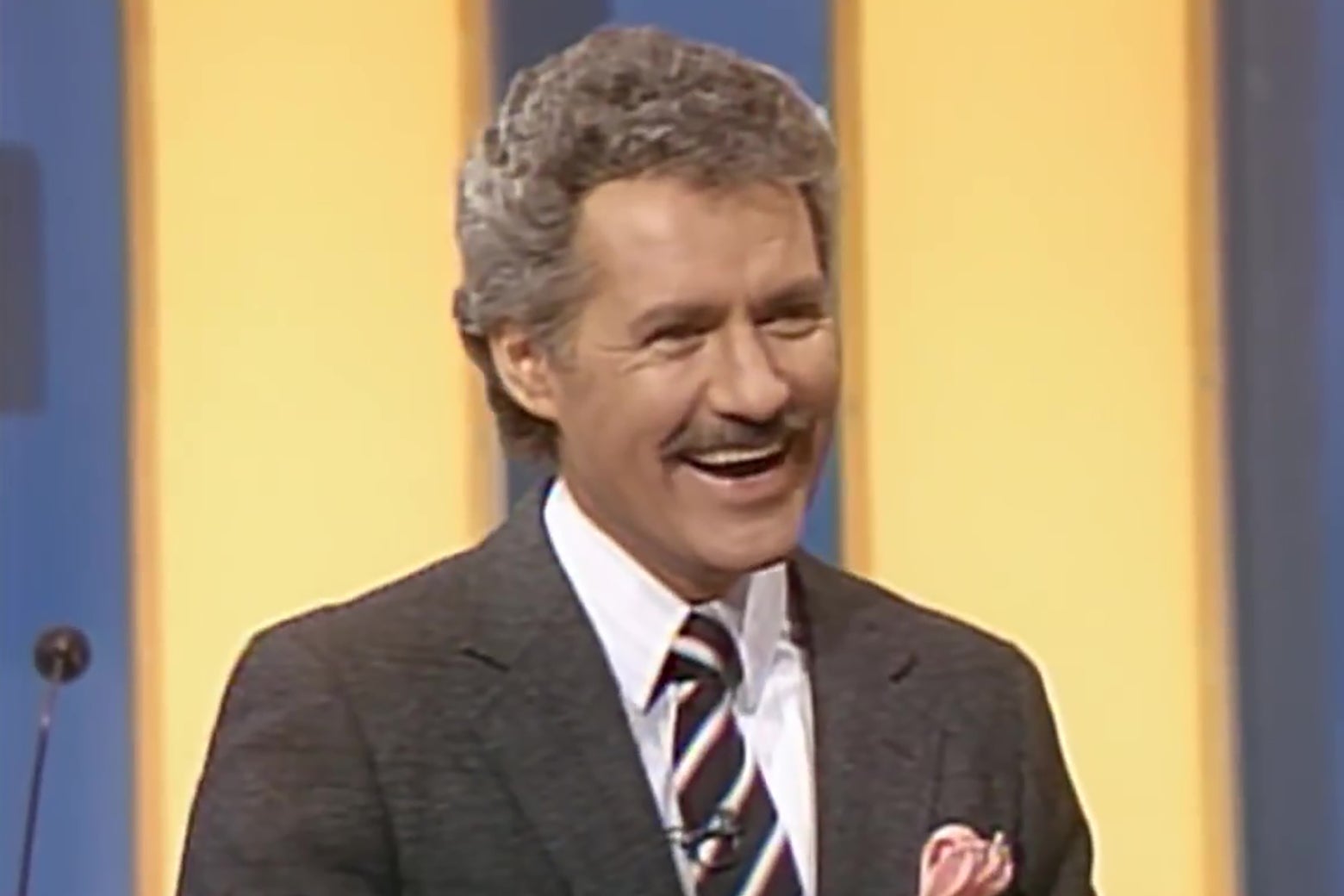 Alex Trebek, circa the 1980s, smiling broadly on the set of Jeopardy.