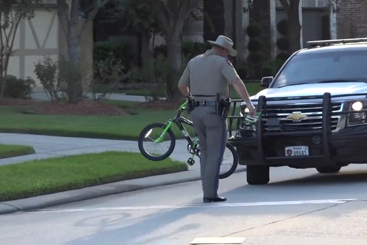 A police officer carries a small bike to his car.