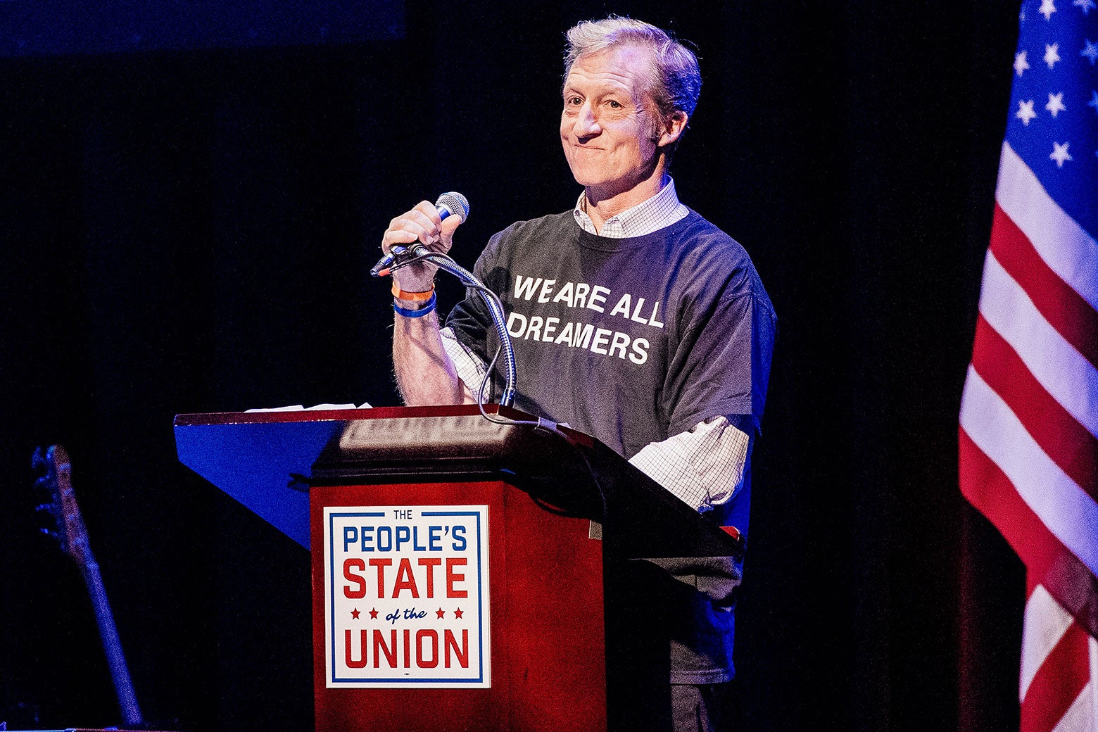 Tom Steyer, wearing a shirt that says, "We are all Dreamers," stands at a podium.