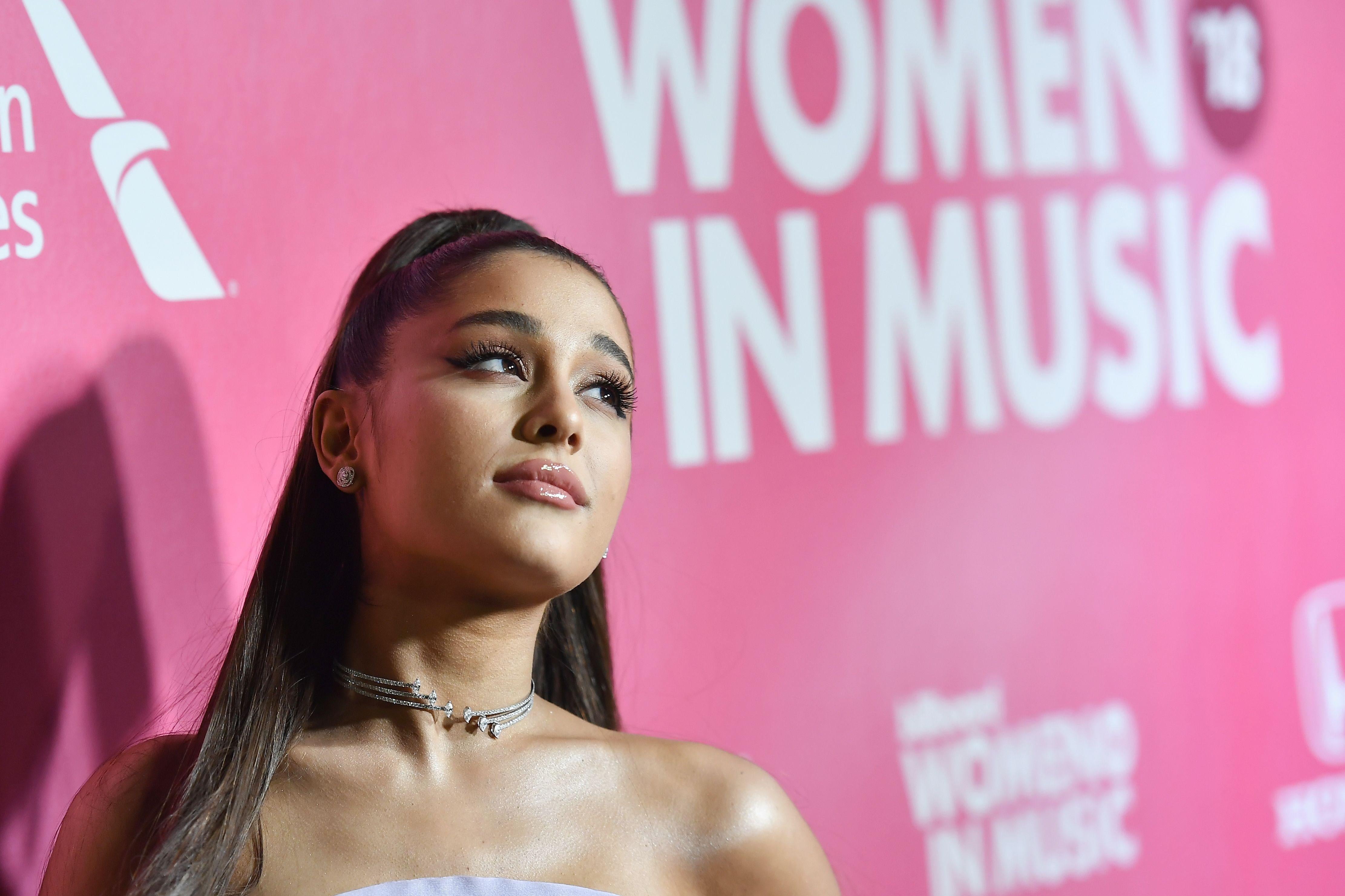Ariana Grande stands in front of a pink background that says "Women in Music."