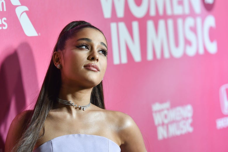 Ariana Grande stands in front of a pink background that says "Women in Music."