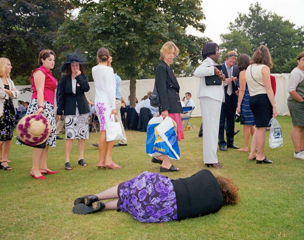 A woman lies on the grass next to a queue for the toilet at the Henley Royal Regatta. 