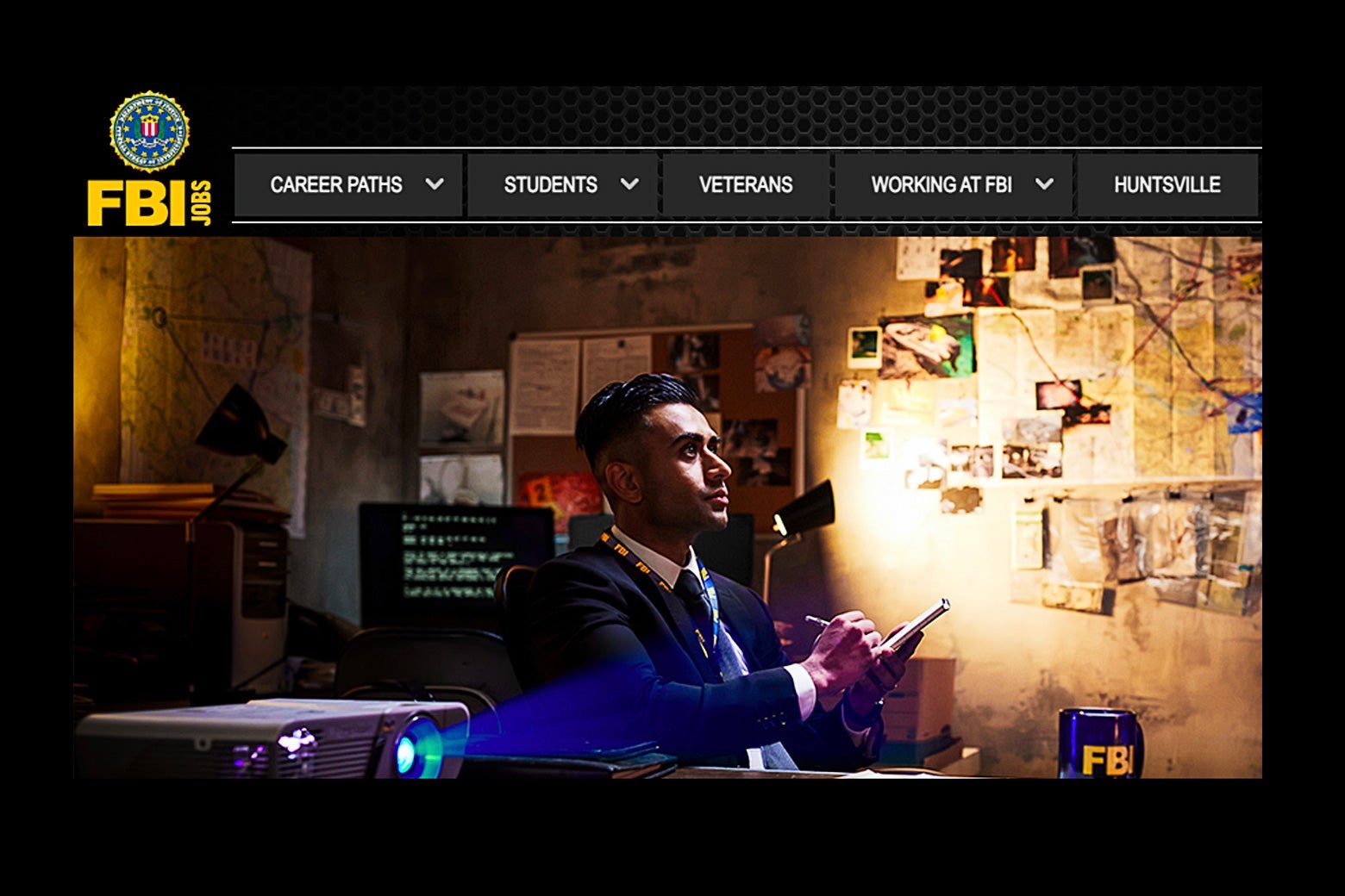 Screenshot of an FBI website with a photo of an agent taking notes as he sits next to a projector and a wall covered in pictures and clues connected with string