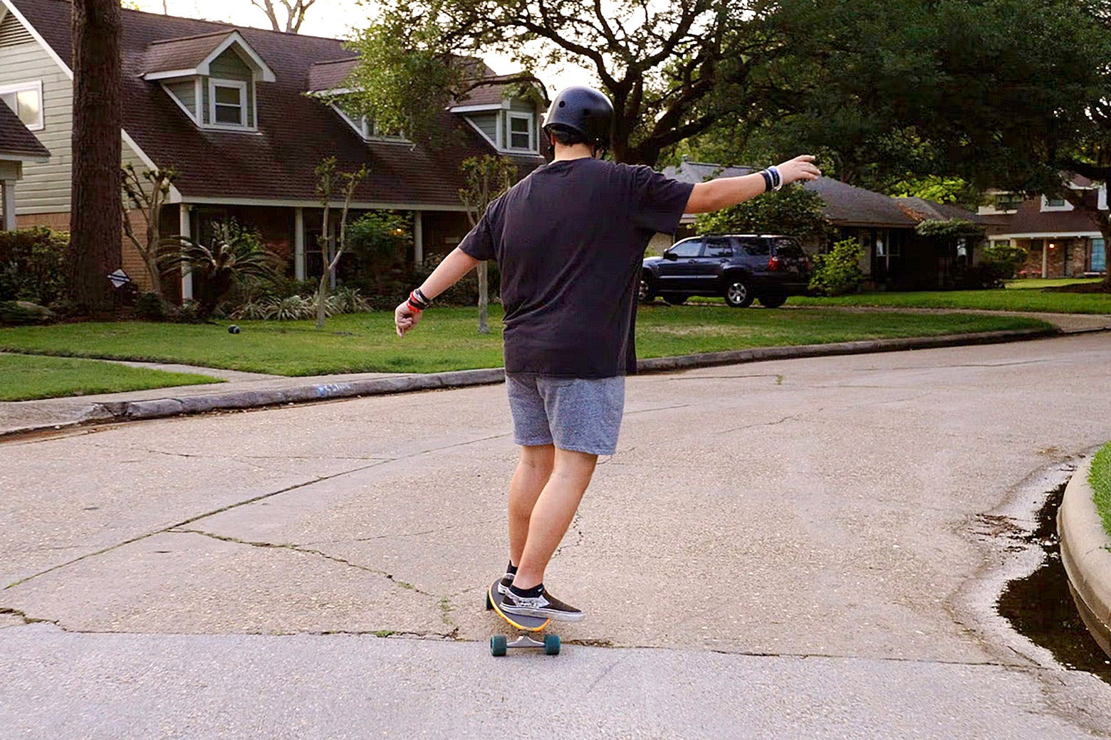 Noah is shown from the back skateboarding down a suburban street.