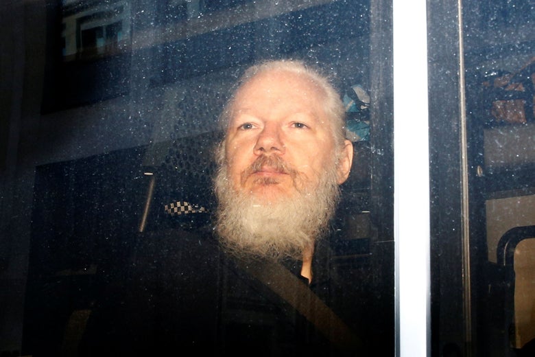 Julian Assange, bearded, seen through a van window.