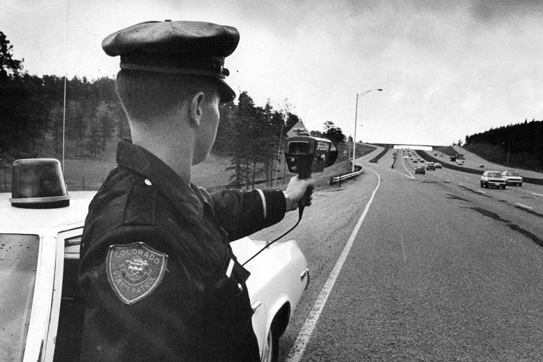 A state trooper holding a radar gun next to a highway.