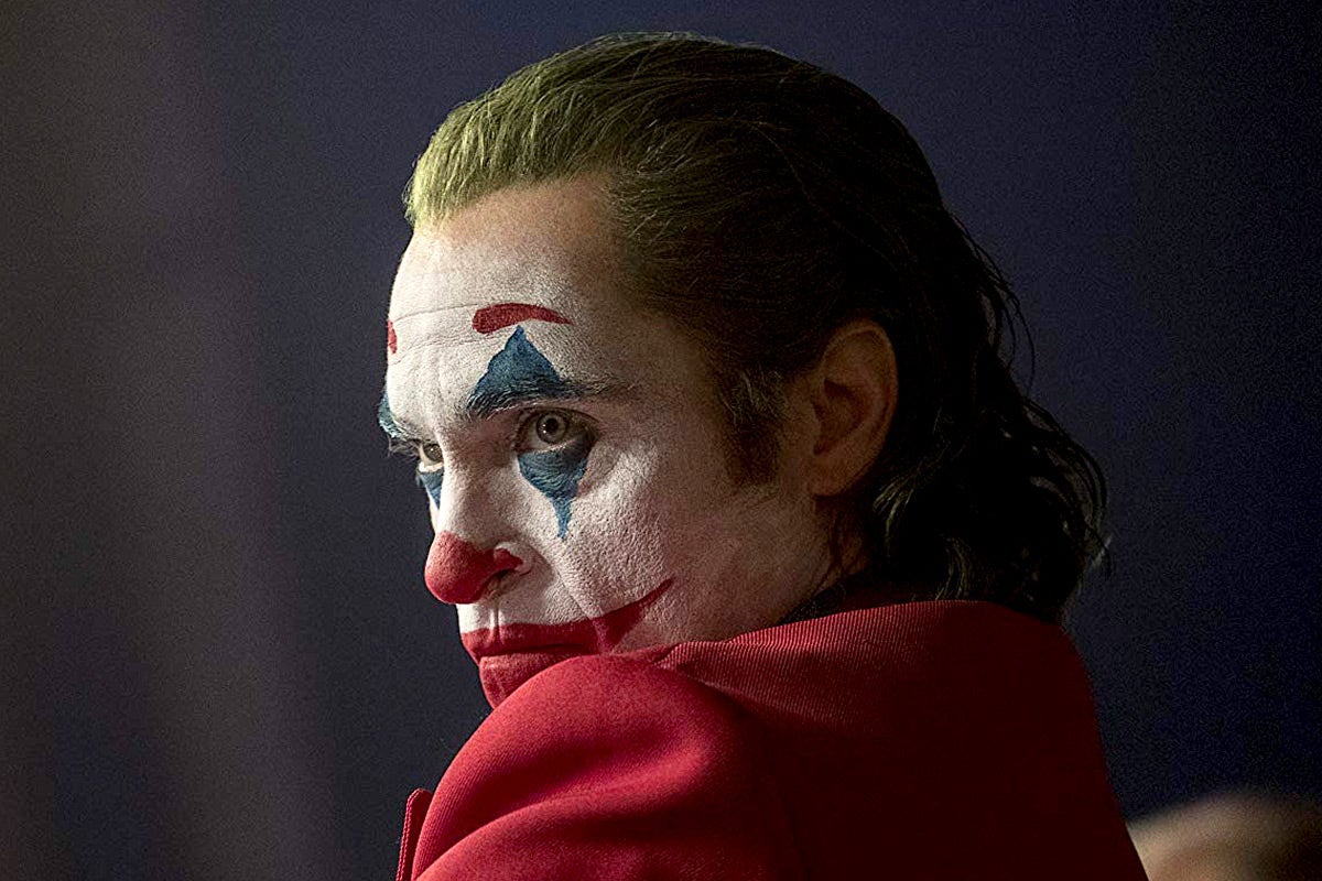 Joaquin Phoenix, in profile, in a red suit and clown makeup.