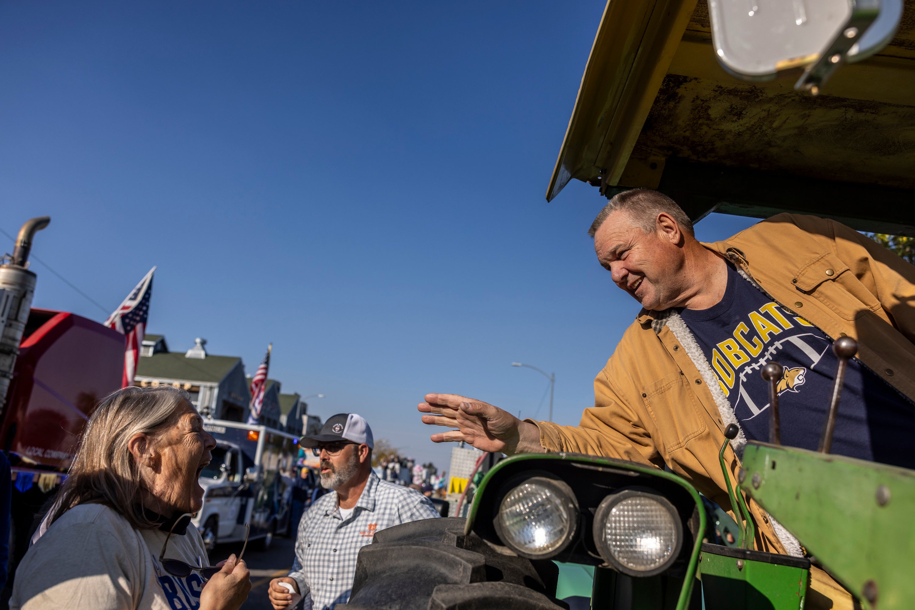 A white man with a flattop haircut waves to a grinning woman from a tractor.