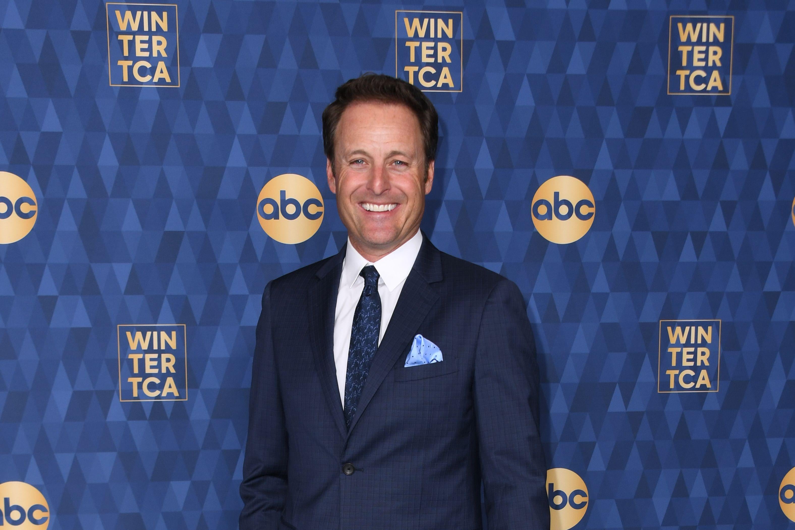 Chris Harrison in a suit standing in front of an ABC step and repeat.