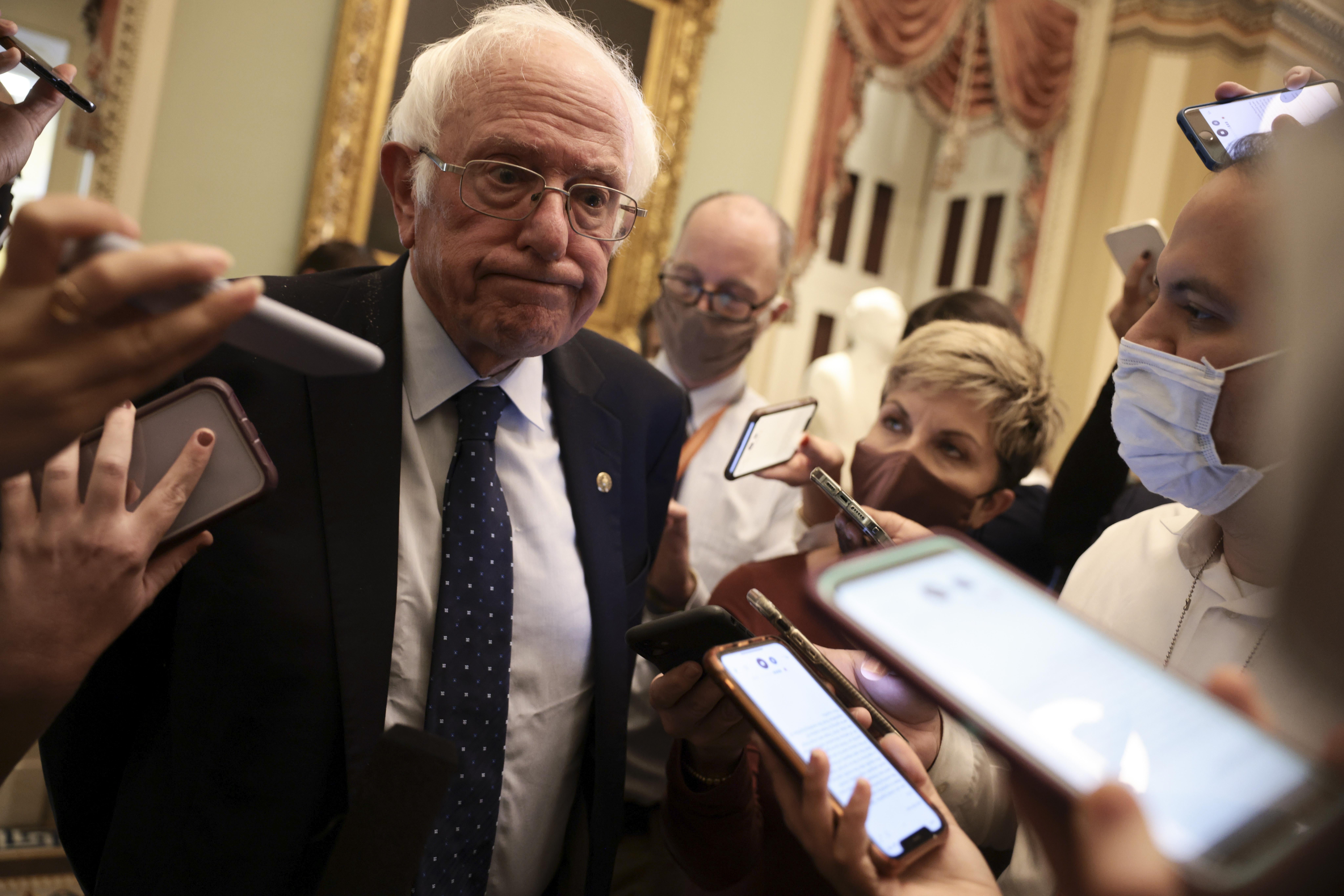 Bernie, surrounded by reporters holding phones, looking puzzled