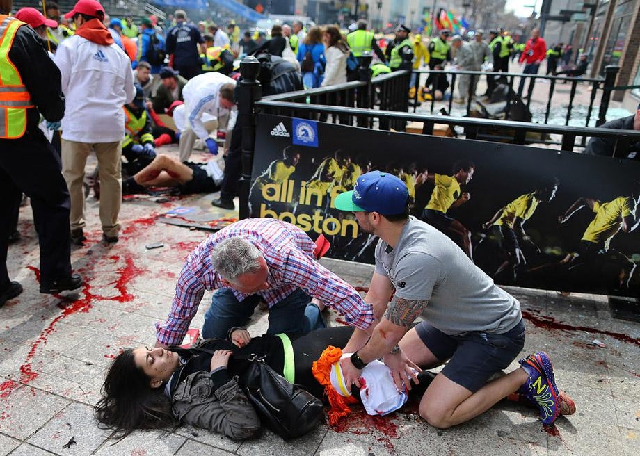 Bystanders help an injured woman at the scene of the first explosion on Boylston Street near the finish line of the 117th Boston Marathon.