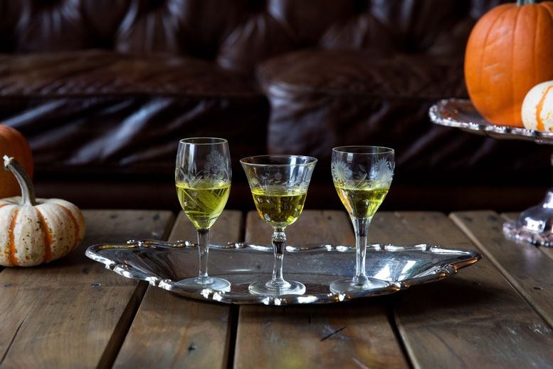 Three glasses of Strega on a metal platter, with decorative pumpkins on either side of the platter