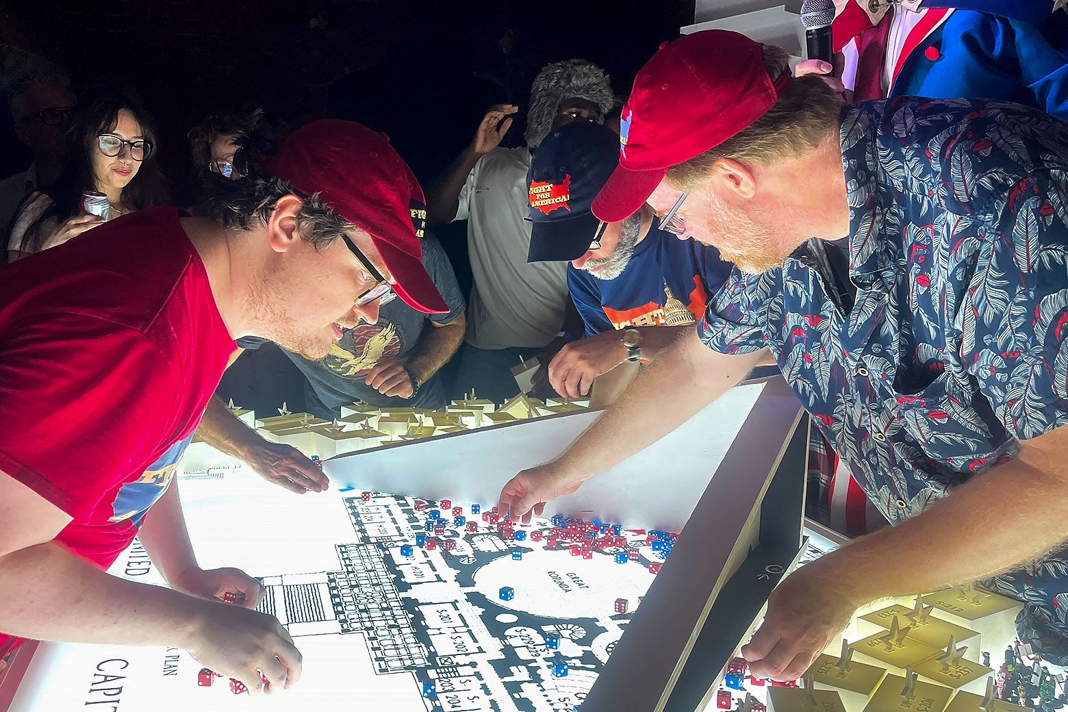 People lean over a lit-up display in the game board and talk to each other.