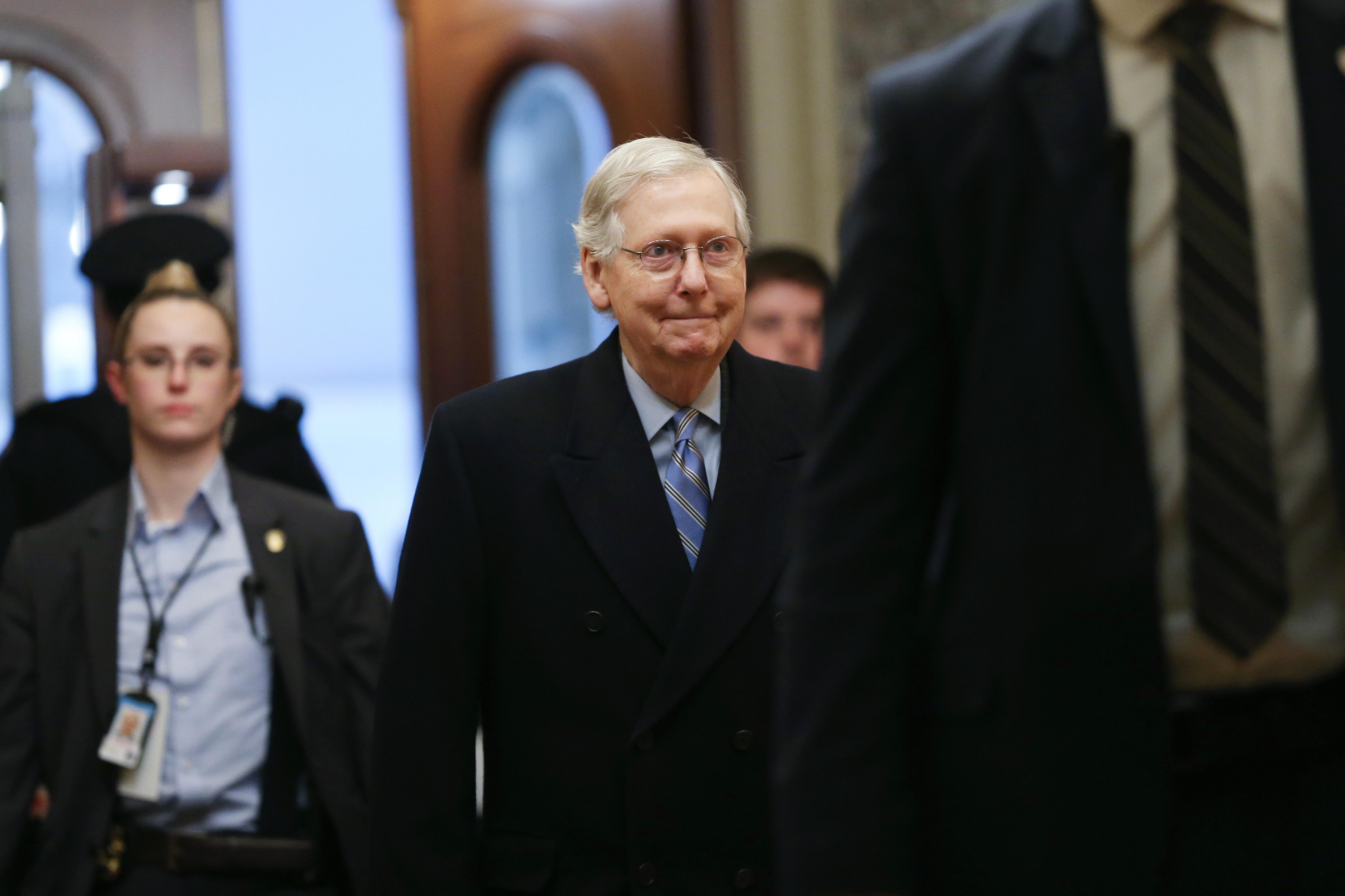 Mitch McConnell walks with aides behind him.