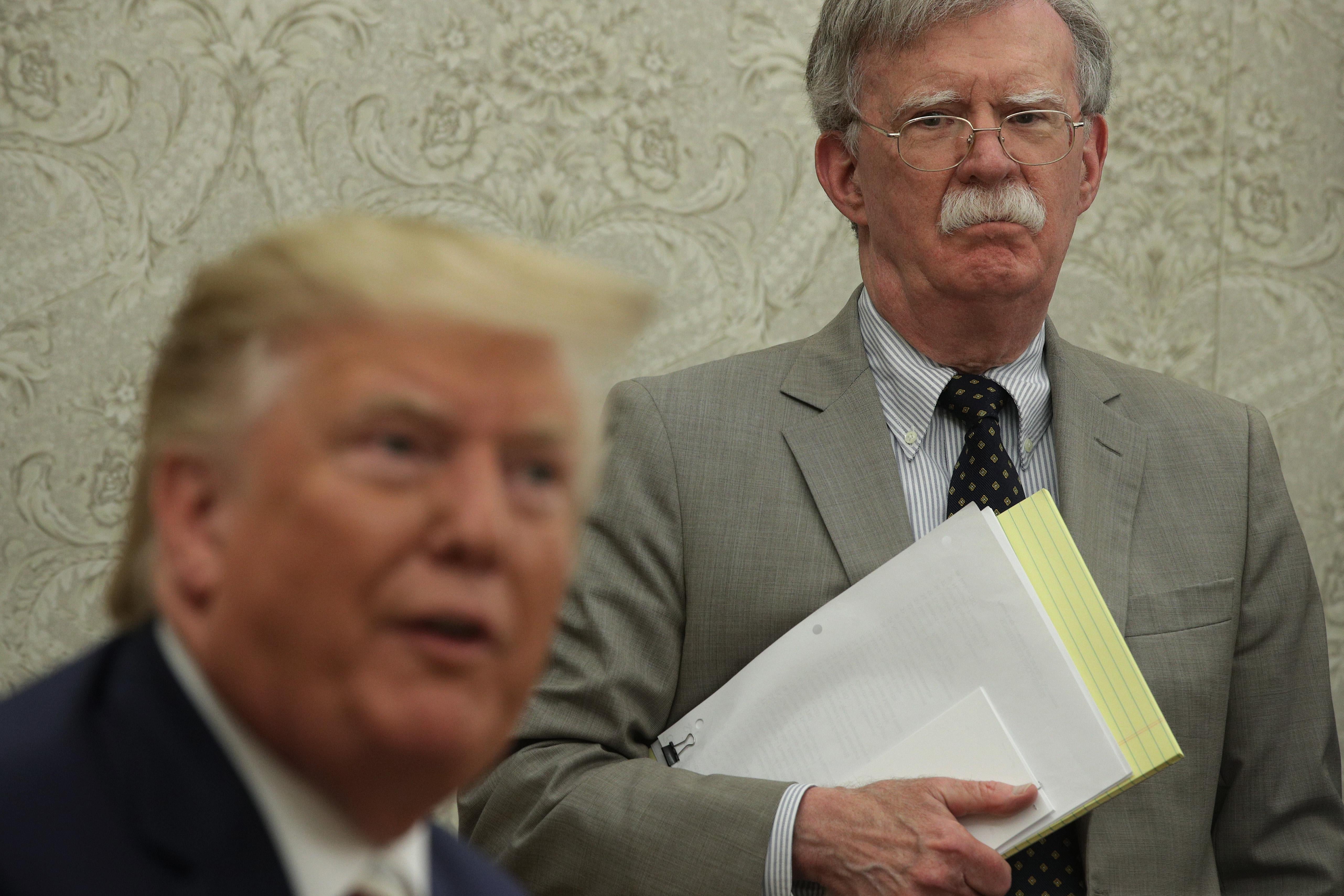 Bolton holding papers and looking at Trump, who is speaking.