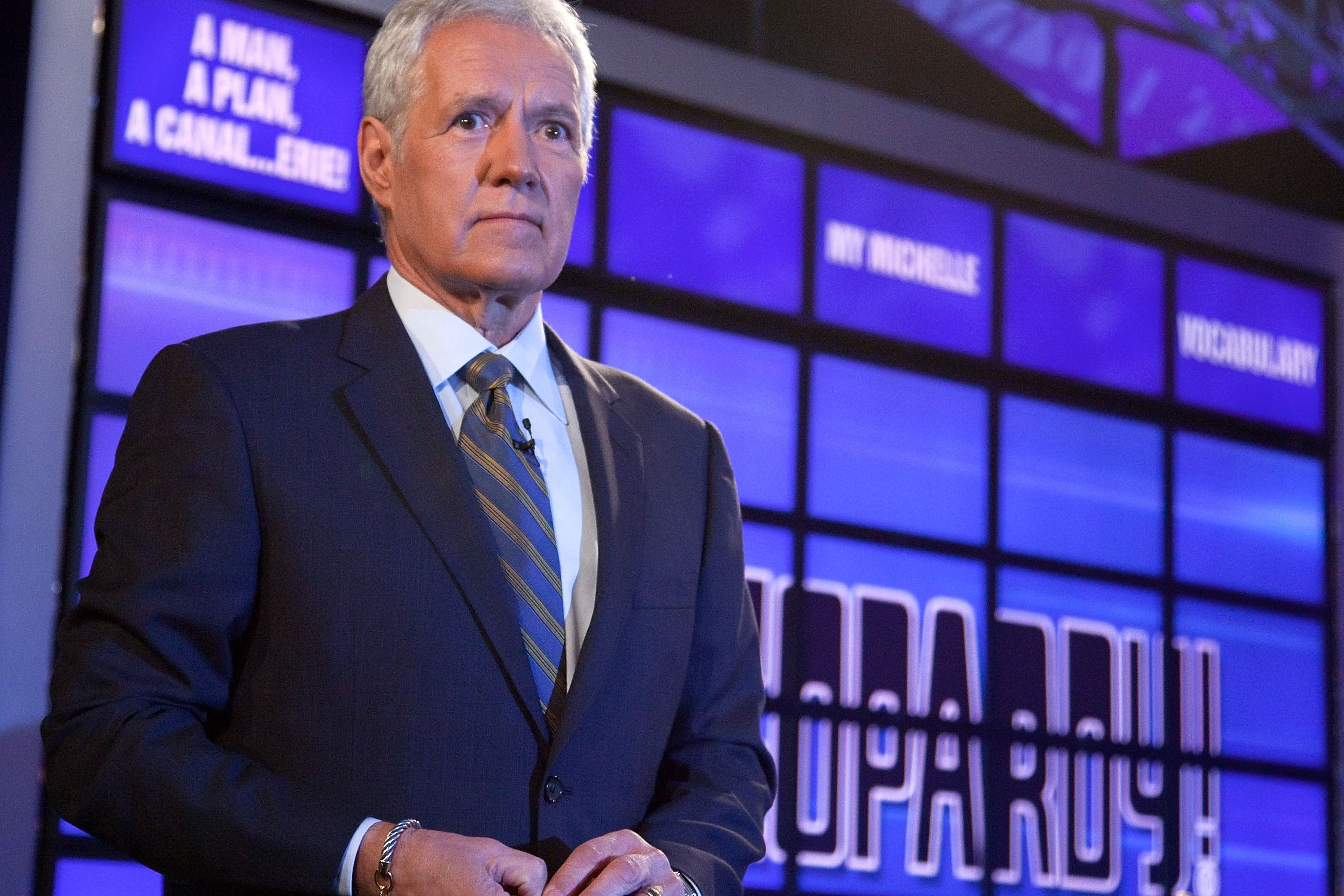 Alex Trebek looking serious and staring straight ahead on the set of Jeopardy.