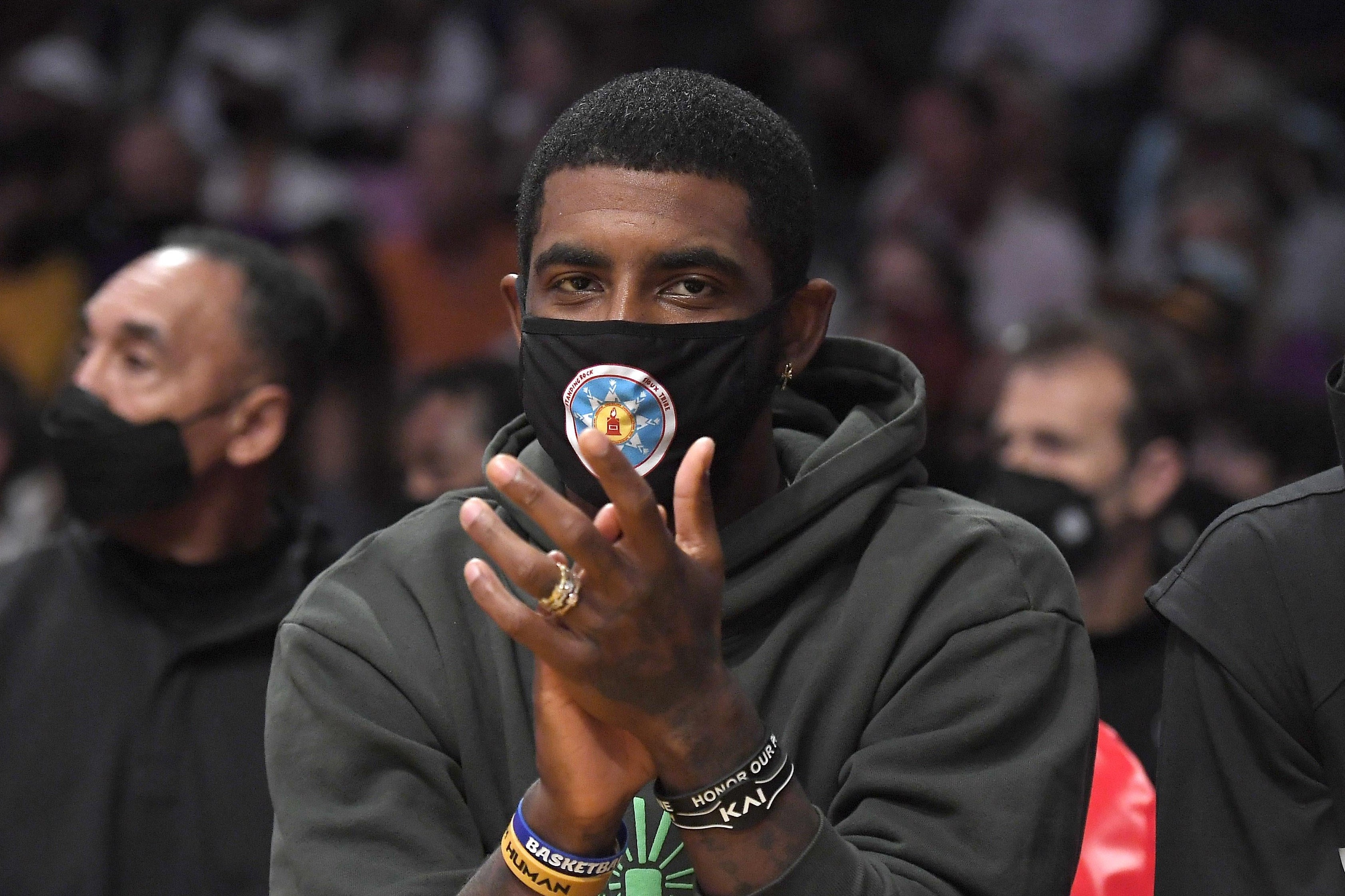 Kyrie seated in a hoodie and mask applauding.