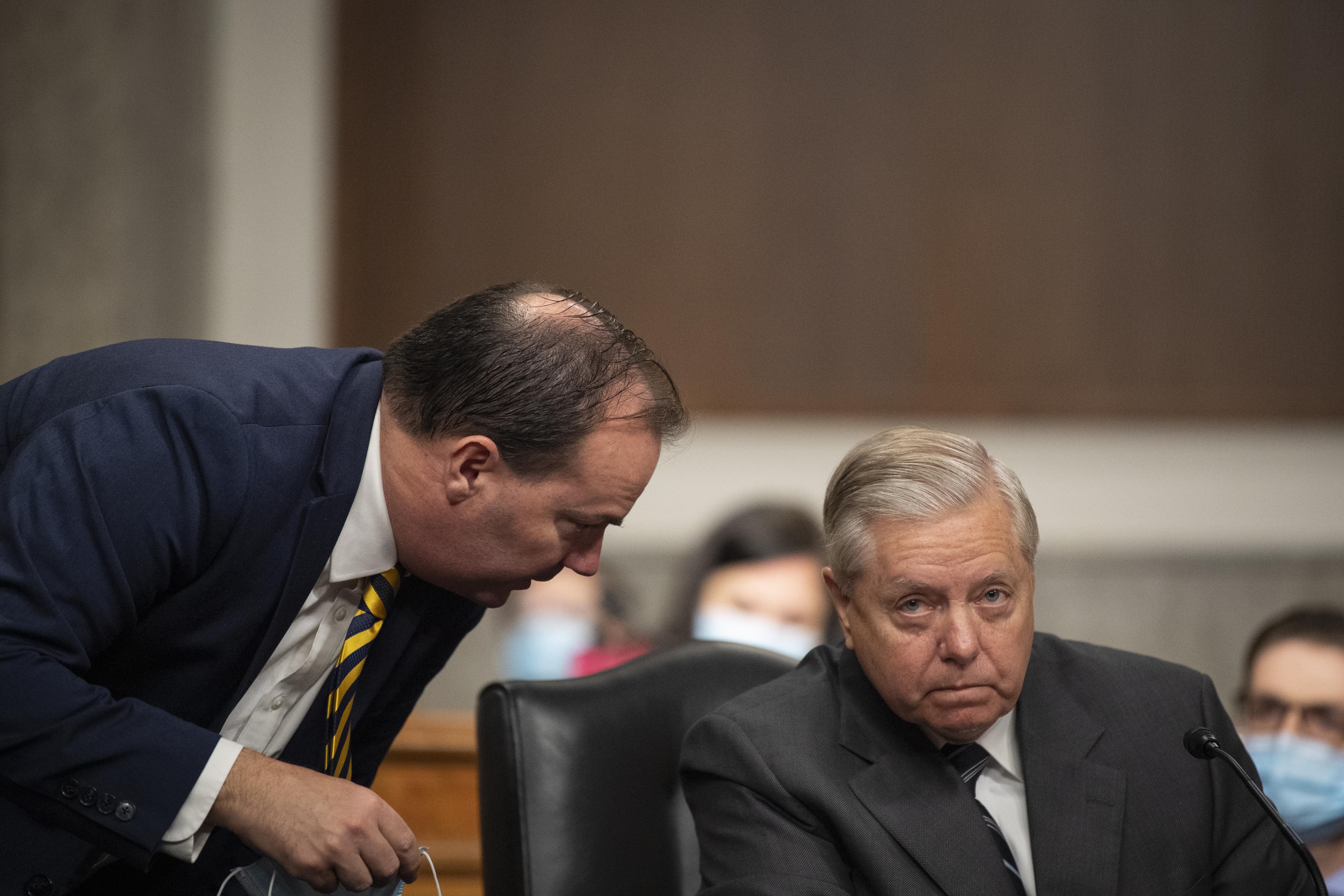 Lee, standing, leans in to speak with Graham, seated