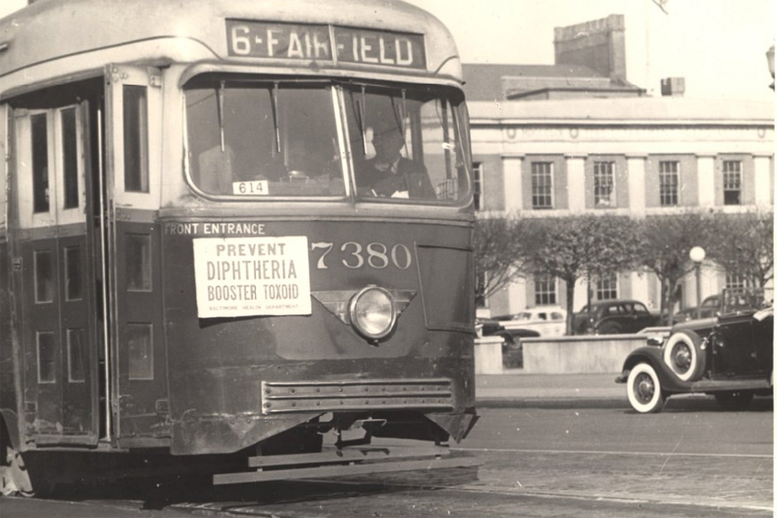 A bus has a sign on the front of it that says, "Prevent diphtheria booster toxoid."
