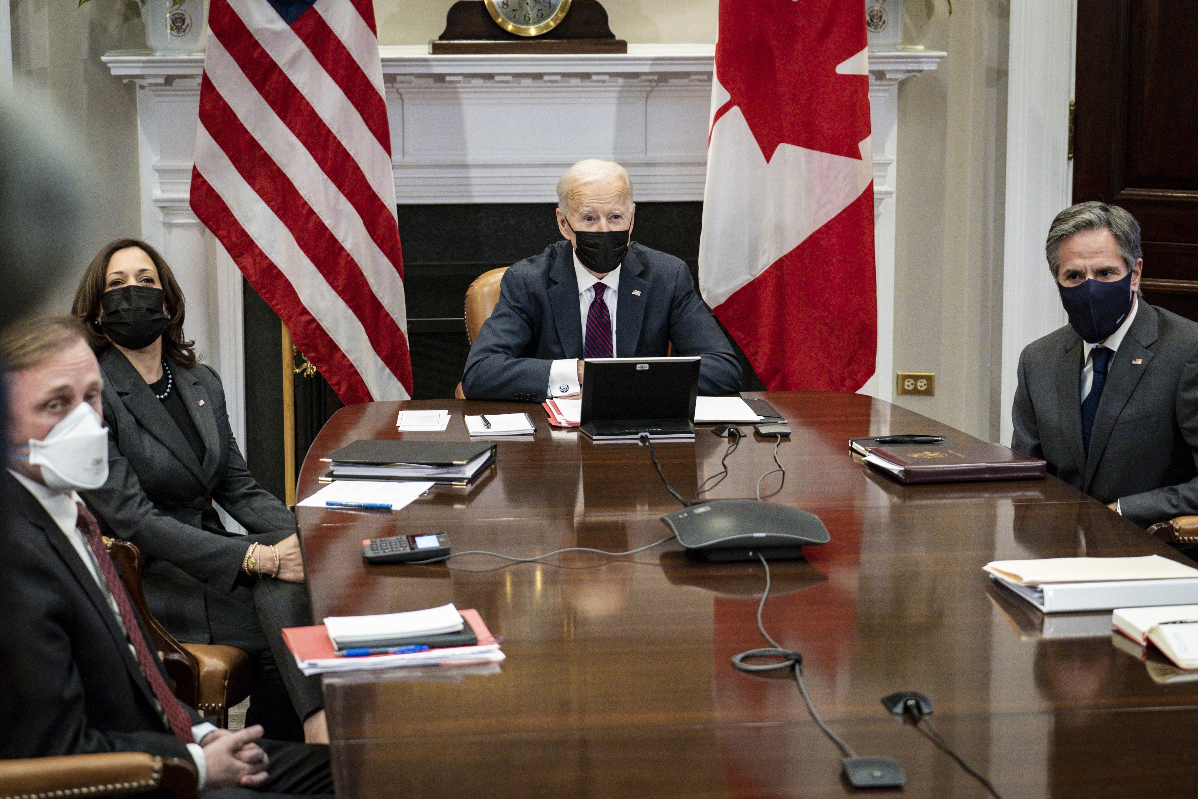 Sullivan, Harris, Biden, and Blinken seated around a conference table, wearing masks