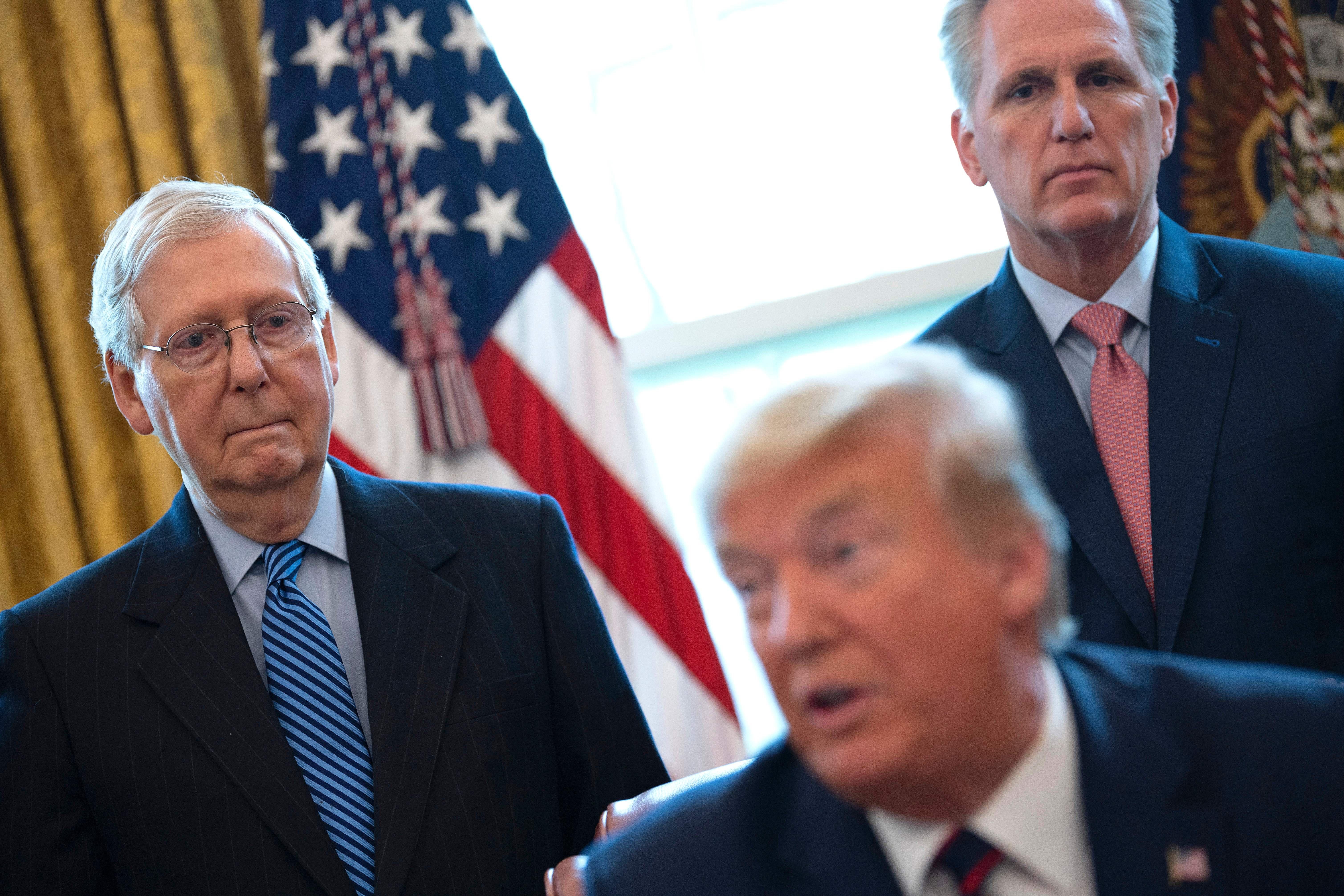 Mitch McConnell and Kevin McCarthy stand behind and look at Donald Trump.
