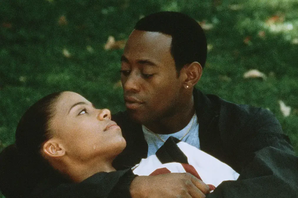 Omar Epps wraps his arms around Sanaa Lathan as they sit on a green lawn. 
